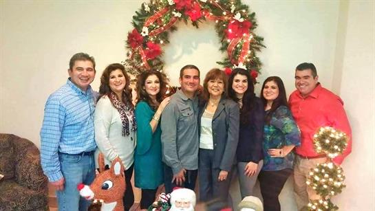 Group of people smiling and posing together in front of a holiday wreath and decorations.