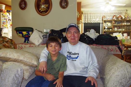 A young boy sits beside his grandfather on a cozy couch, both smiling happily.