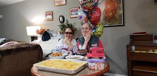 Friends enjoy a birthday celebration surrounded by tasty dishes and colorful balloons while smiling.