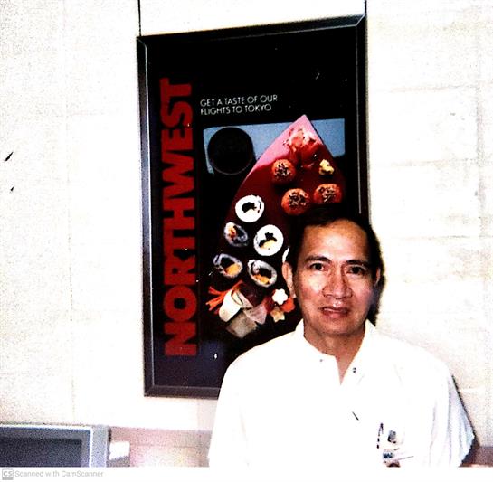 A chef poses before a colorful poster displaying diverse, creative dishes.