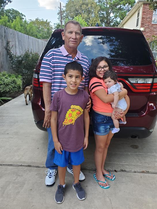 Family enjoys outdoor summer time, with kids playing and a baby being held.