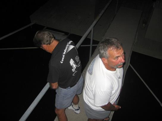 Two men are focused on fishing from a dock in a peaceful, starry night setting by the water.