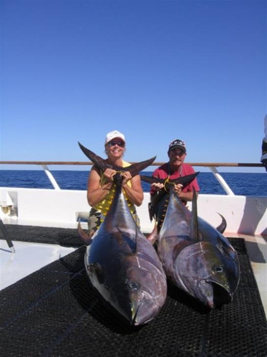Anglers celebrate a successful fishing trip by holding up their impressive tuna catches on deck.