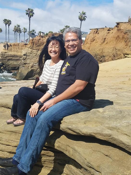 Two people relax on a rocky beach, smiling and enjoying the warm weather by the ocean.