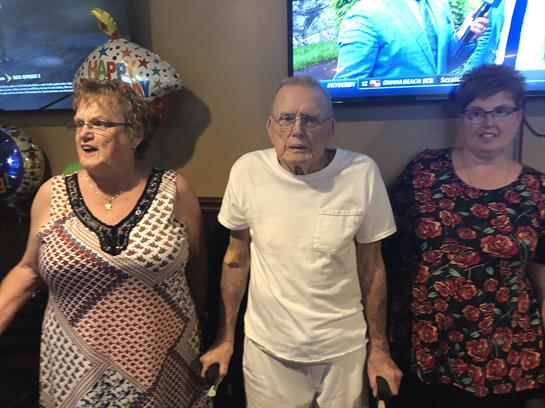 Three individuals participate in a birthday celebration, showcasing joy and togetherness.