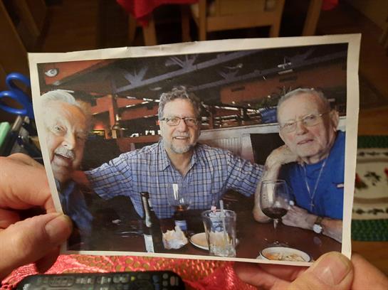 Group of three men smiling at a restaurant table while enjoying drinks and food together.