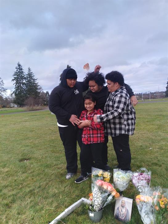 Four family members stand together in a park, sharing a moment with flowers on the ground.