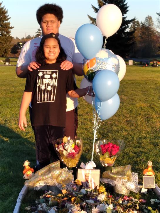 A group honors a special memory with balloons and flowers in a sunset park.