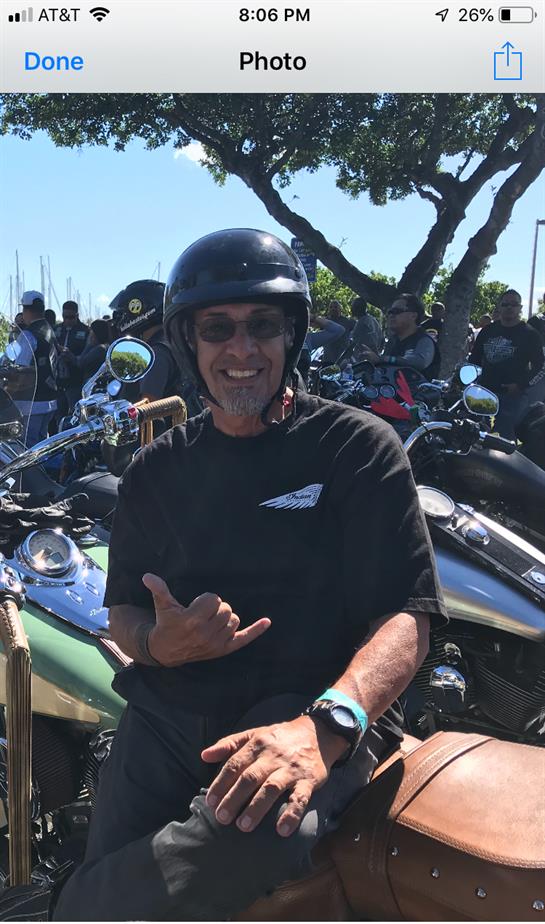 A biker smiles on their motorcycle at a sunny gathering of fellow motorcycle enthusiasts.