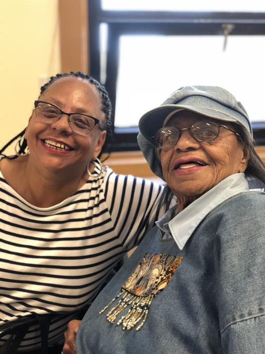 Two women enjoy a warm moment, sharing smiles in a lively indoor atmosphere with family.