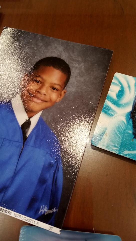 A young boy wearing a blue graduation gown smiles proudly in his school portrait.