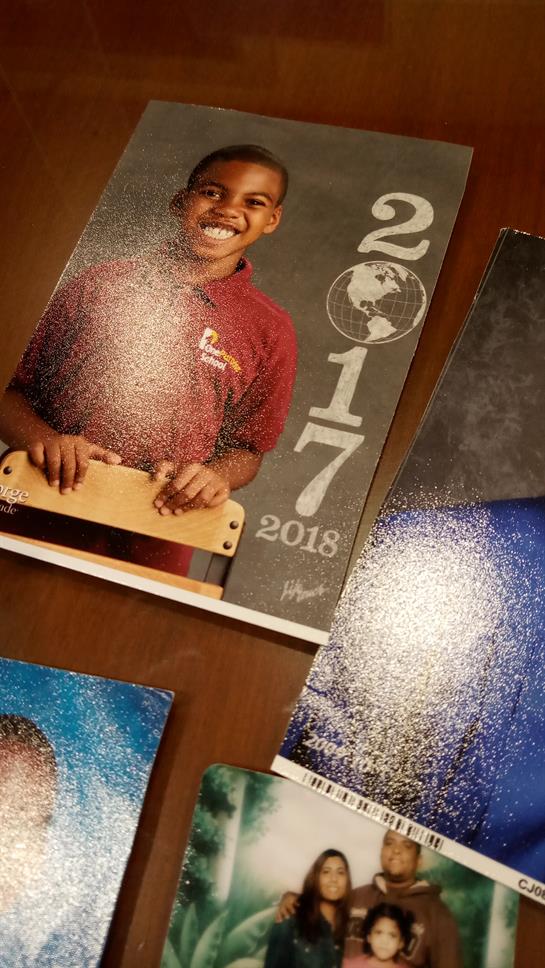 A boy in a maroon shirt smiles while holding a wooden toy in a classroom display.