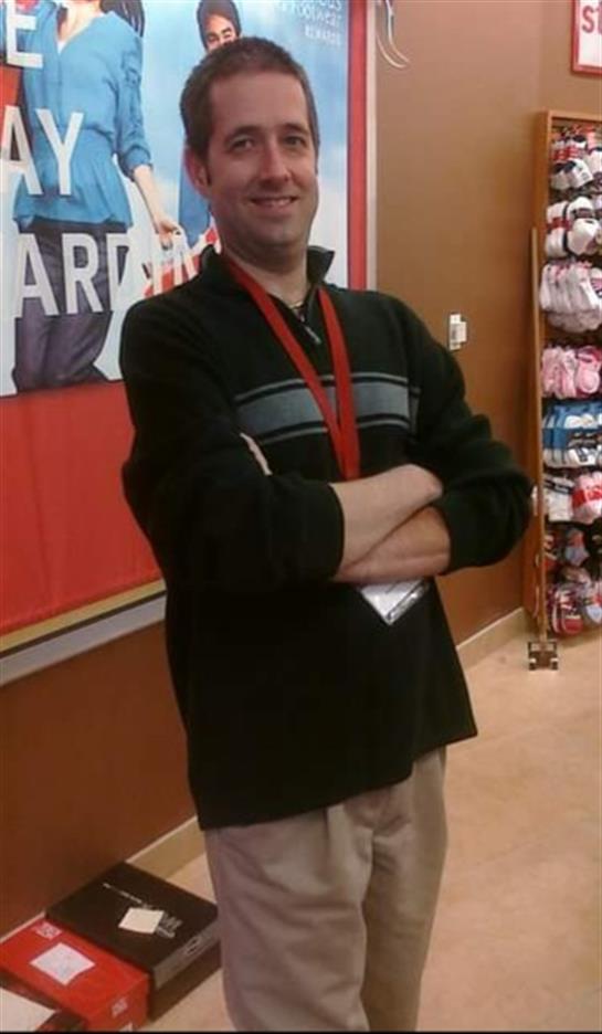 Individual stands in a shop, arms crossed, displaying a confident demeanor amidst various products.