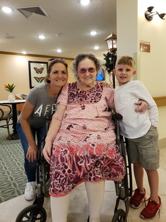 A woman and a child share a joyful moment with an elderly resident in a cozy care facility.