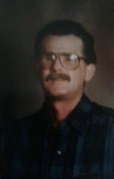 A middle-aged man wearing glasses smiles gently, radiating warmth and kindness in soft lighting.