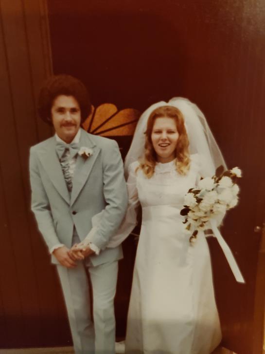 Newlyweds proudly pose outside a venue, showing off their joy and wedding outfits.