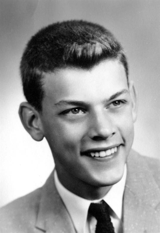 A young man is smiling confidently, dressed in a formal suit, showcasing neatly styled hair.