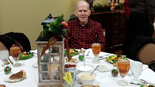 Senior man smiles while seated at a beautifully arranged table with holiday dishes.
