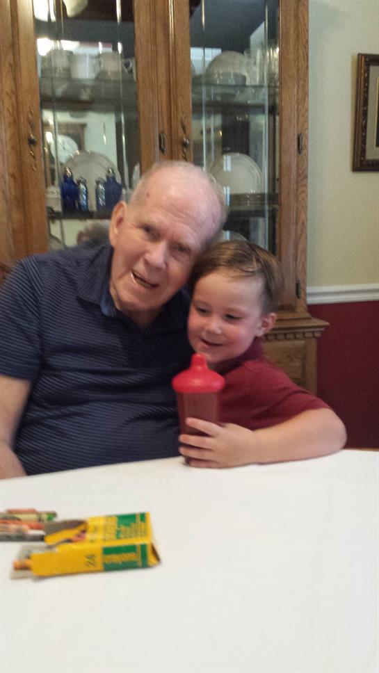 A grandfather and his young grandson smile affectionately while sitting at a table together.
