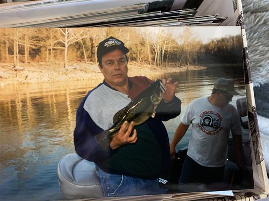 Two men enjoy fishing on a lake, one holding a large catch while smiling at the camera.