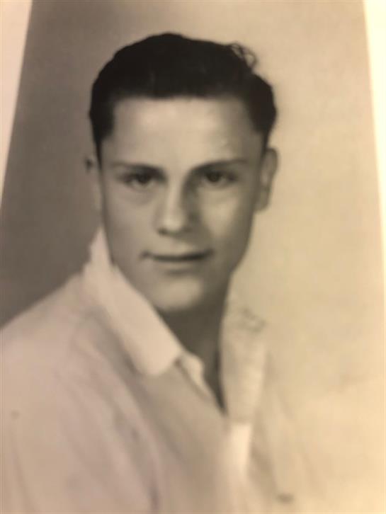 A young man with dark hair is posing for a portrait in a simple studio environment.