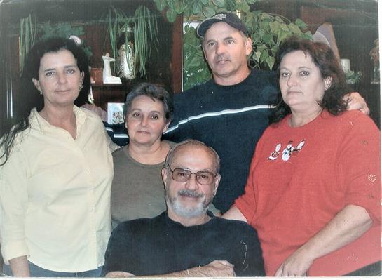 Five adults stand and sit closely together in a warm, inviting living room filled with plants.