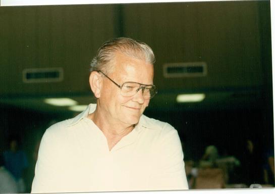 A cheerful elderly man wearing glasses enjoys a social gathering with warm lighting.