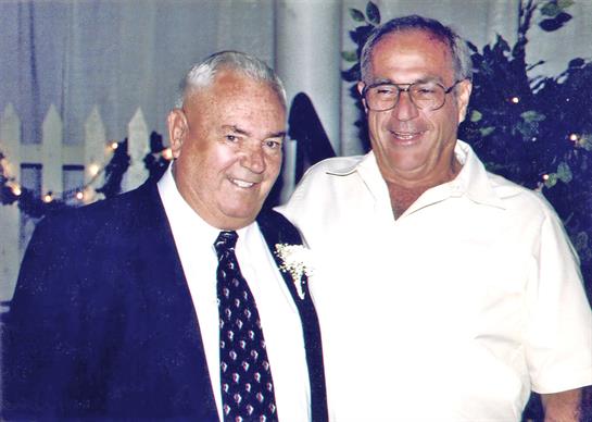 Two men smile warmly while enjoying a joyful moment at a festive event filled with decorations.