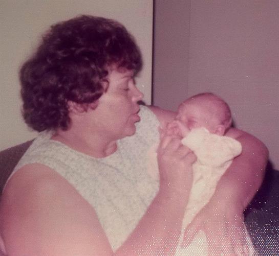 A grandmother gently feeds her baby grandchild while seated in a comfortable living room.