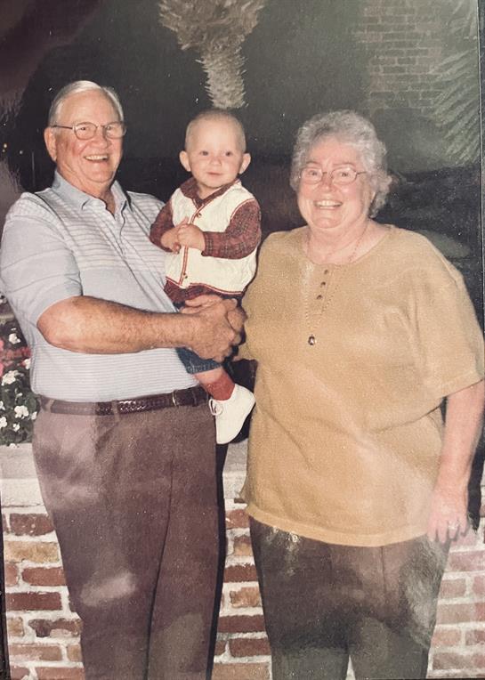 Two grandparents warmly embrace their grandchild in a close family moment indoors.