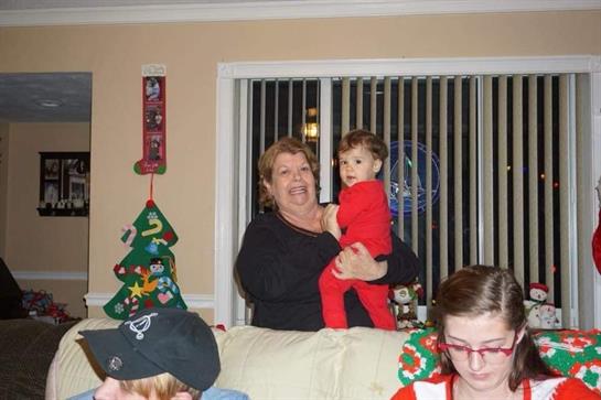 A cheerful elder woman holds a young child in red while others enjoy their time together.