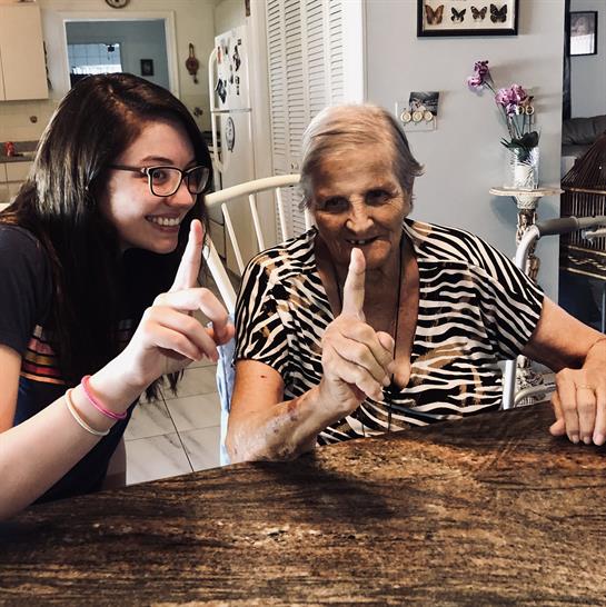 Two women smile and hold up their index fingers in a fun gesture, enjoying each other's company.