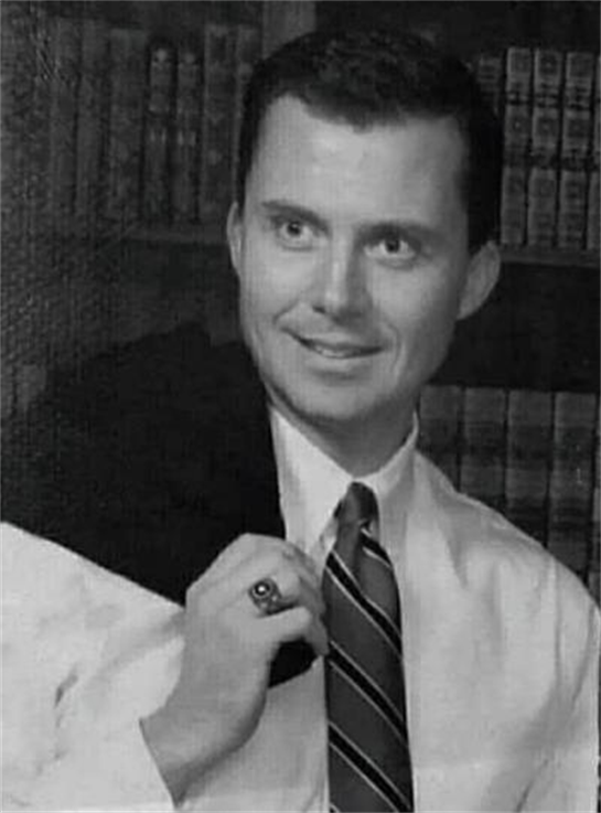 A young man poses in a suit with a jacket on his shoulder, smiling in a vintage library.