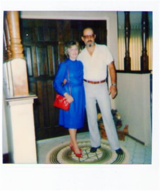 A couple stands smiling elegantly by their home entrance.