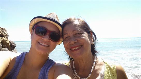 Two women pose happily at the beach on a sunny day, sharing a joyful moment and smiles.