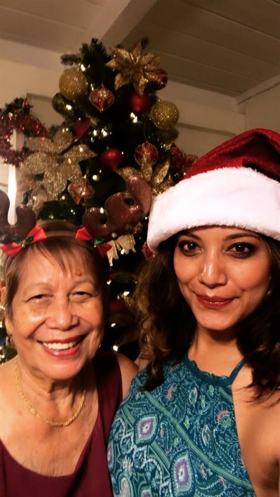 Two women happily pose in festive attire near a Christmas tree adorned with decorations.