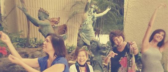 Friends laugh and share joyful moments while posing near a vibrant statue in a lush garden.