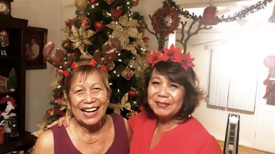Two friends wearing festive headbands smile brightly in a decorated holiday setting.