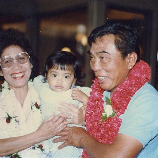 A joyful family in Hawaii with parents proudly holding their baby in colorful leis.