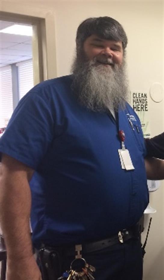 A bearded staff member assists visitors in a hospital corridor.