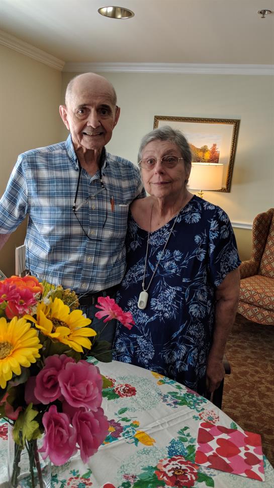 Happy elderly couple stands by a table with vibrant flowers, celebrating together.