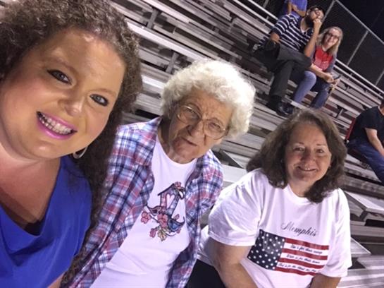 Three women pose happily together in a stadium, enjoying the excitement of a local sports event.