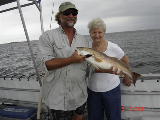A fisherman and a woman hold a large fish together on a boat in the sea.