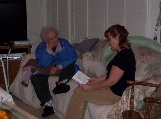 A woman sits across from an elderly man, sharing a thoughtful conversation in a cozy living room.
