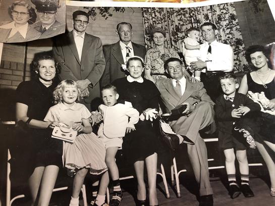 A large family is gathered in a cozy setting, showing smiles and interactions typical of the era.