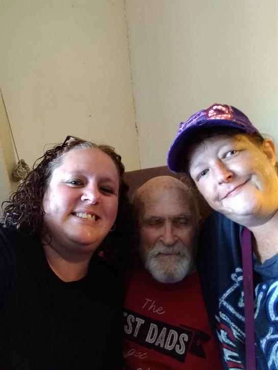 Two women enjoy time with an elderly man, smiling and capturing the moment in a warm setting.