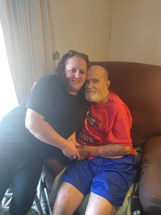 A caregiver sits with an elderly man in a relaxed posture, promoting companionship and warmth.
