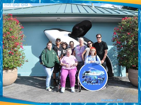 A group of family members poses joyfully in front of an orca statue at a marine attraction.