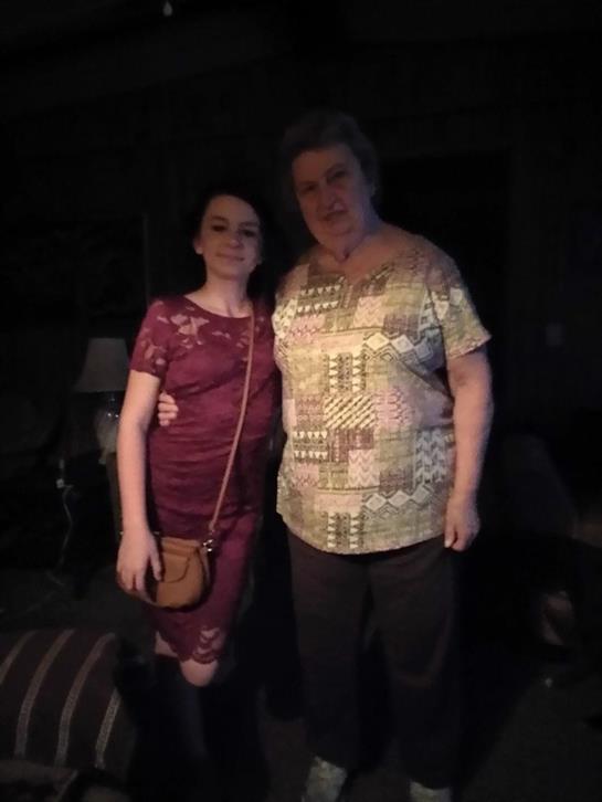 Two people stand closely together, smiling warmly in a relaxed indoor space at night.