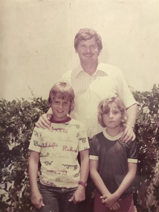 A happy father enjoys a warm moment with his two kids in a sunny green setting.